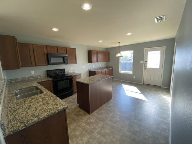 kitchen with brown cabinetry, a kitchen island, light stone counters, black appliances, and a sink