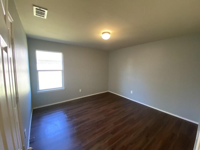 unfurnished room with visible vents, dark wood finished floors, and baseboards