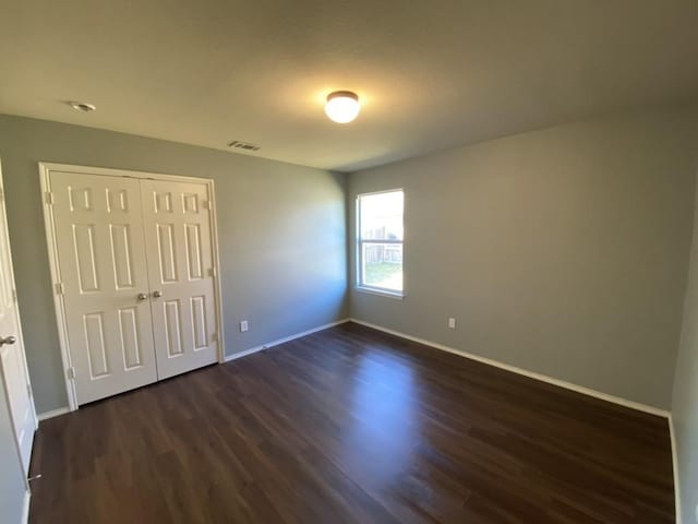 unfurnished bedroom with baseboards, a closet, visible vents, and dark wood-type flooring