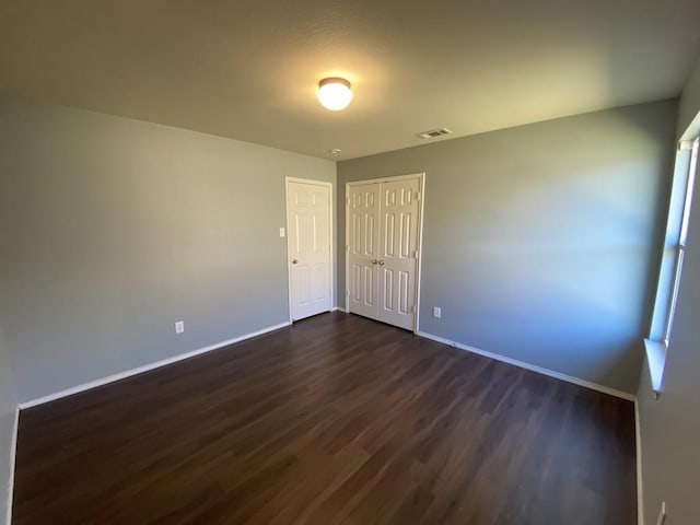 empty room with dark wood finished floors, visible vents, and baseboards