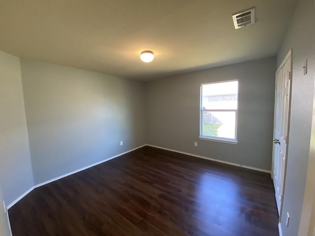 unfurnished room featuring dark wood-style flooring, visible vents, and baseboards