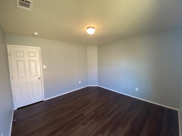 empty room featuring visible vents, dark wood finished floors, and baseboards