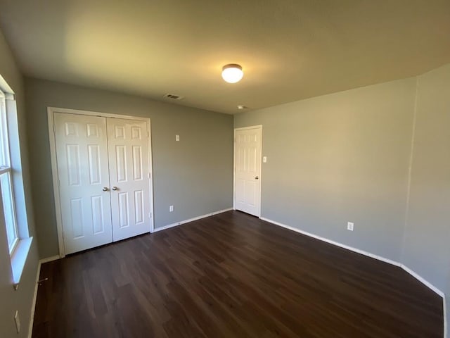 unfurnished bedroom with baseboards, a closet, visible vents, and dark wood-type flooring