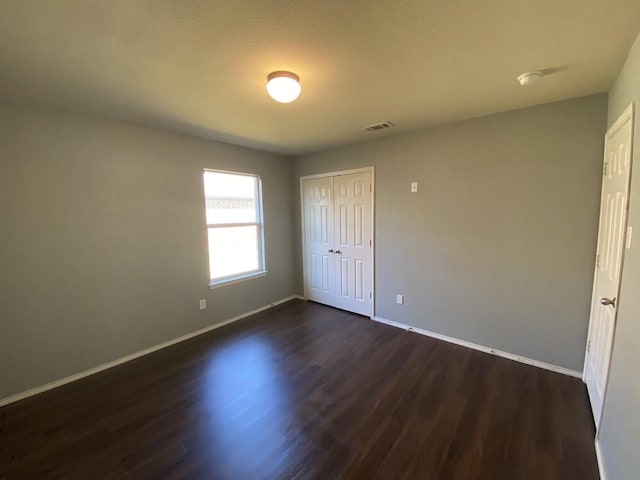 unfurnished bedroom featuring visible vents, a closet, baseboards, and dark wood-style flooring