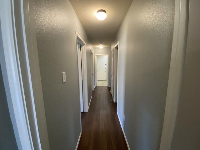 hallway with dark wood-style floors, a textured wall, and baseboards