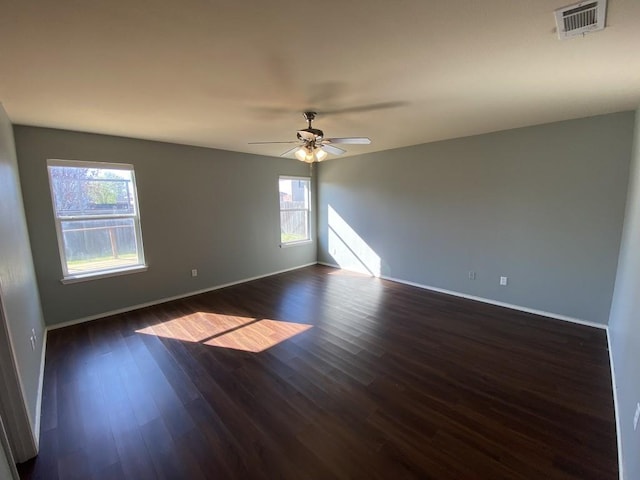 empty room with dark wood-style floors, visible vents, baseboards, and a ceiling fan