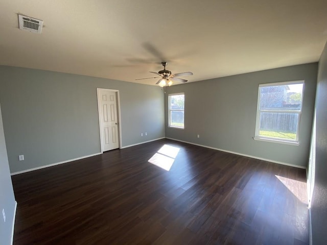 empty room featuring a healthy amount of sunlight, baseboards, visible vents, and dark wood-type flooring