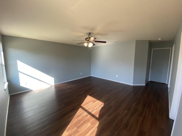 spare room featuring baseboards, ceiling fan, visible vents, and dark wood-style flooring