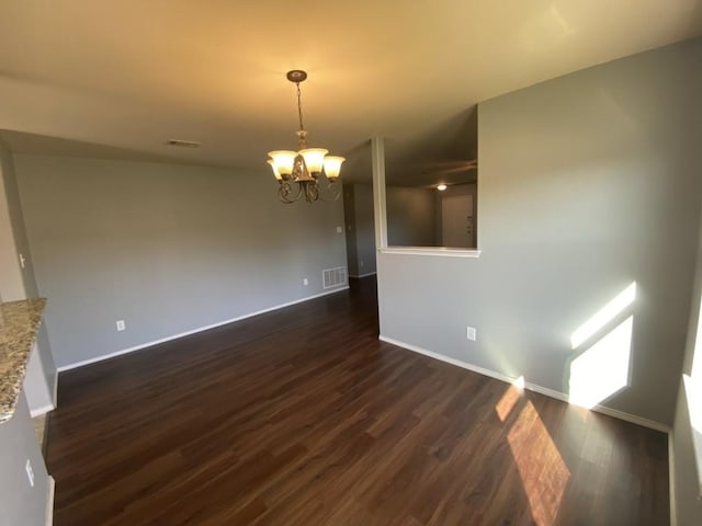 spare room featuring dark wood-style floors, baseboards, visible vents, and a notable chandelier