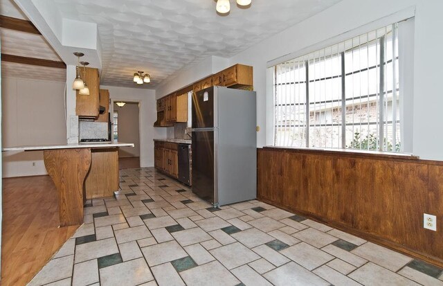 kitchen with a wealth of natural light, freestanding refrigerator, dishwasher, and wooden walls