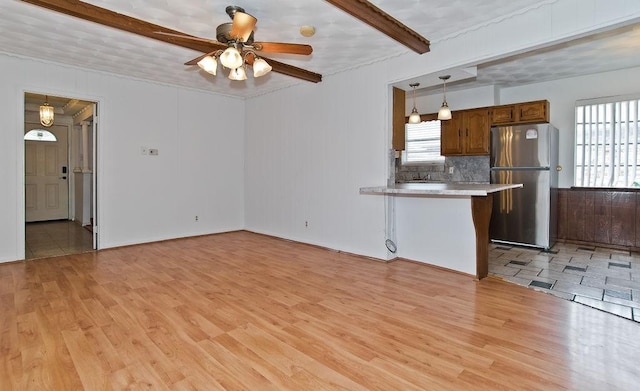 unfurnished living room with a wealth of natural light, light wood-type flooring, and beam ceiling