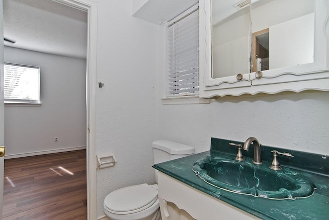 half bath featuring baseboards, vanity, toilet, and wood finished floors