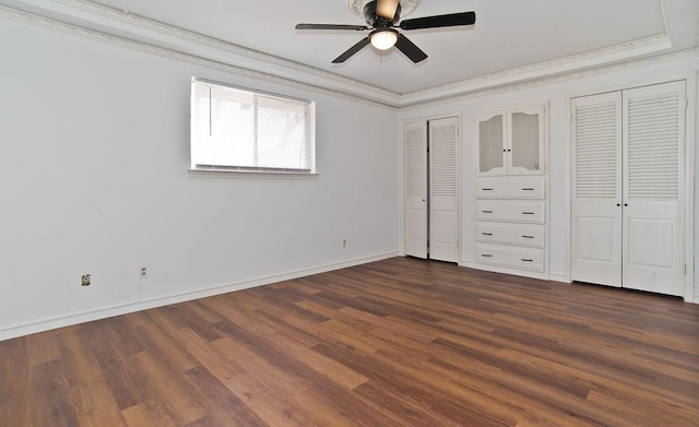 unfurnished bedroom with ornamental molding, dark wood-type flooring, and two closets