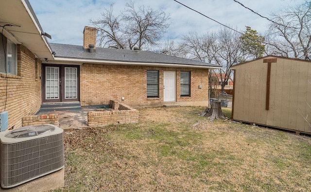 back of property with central AC, brick siding, an outdoor structure, a yard, and french doors