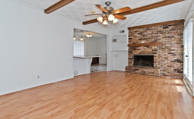 unfurnished living room with visible vents, ceiling fan, wood finished floors, a brick fireplace, and beam ceiling