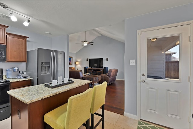 kitchen featuring light stone counters, a center island, visible vents, a ceiling fan, and black appliances