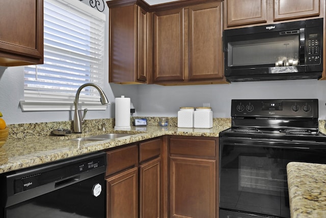 kitchen with light stone counters, a sink, and black appliances