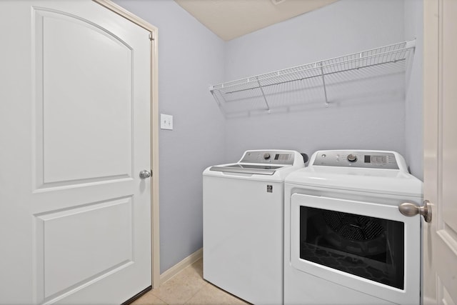 clothes washing area featuring laundry area, baseboards, washer and dryer, and light tile patterned flooring