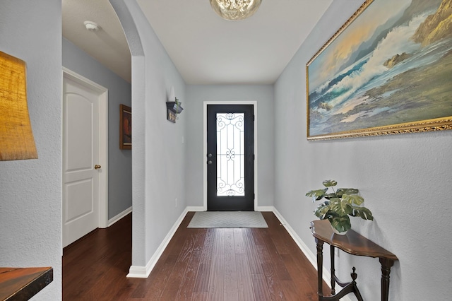 foyer entrance featuring arched walkways, wood finished floors, and baseboards