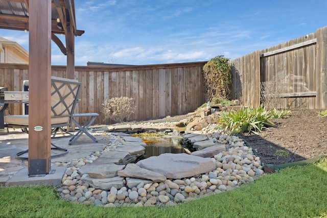 view of yard featuring a patio, a small pond, and a fenced backyard