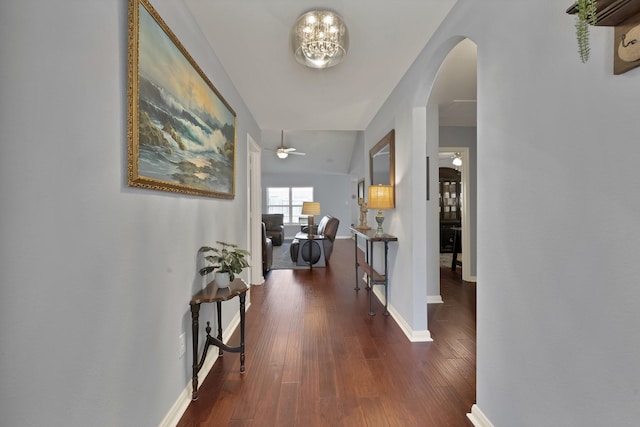 hall featuring an inviting chandelier, baseboards, arched walkways, and wood finished floors