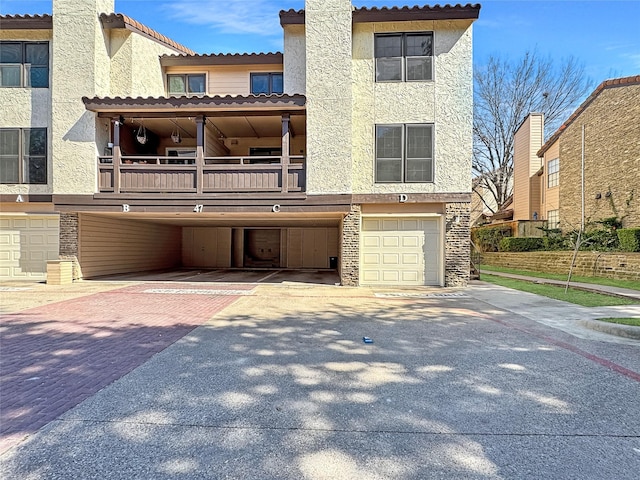 view of front facade with driveway, a balcony, stone siding, an attached garage, and stucco siding