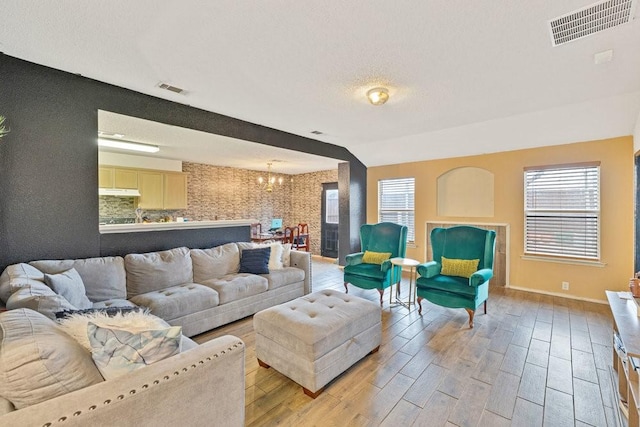 living area featuring a textured ceiling, light wood finished floors, visible vents, and an inviting chandelier