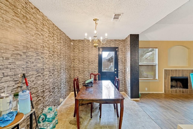 unfurnished dining area featuring visible vents, a tile fireplace, a textured ceiling, light wood-style floors, and a chandelier