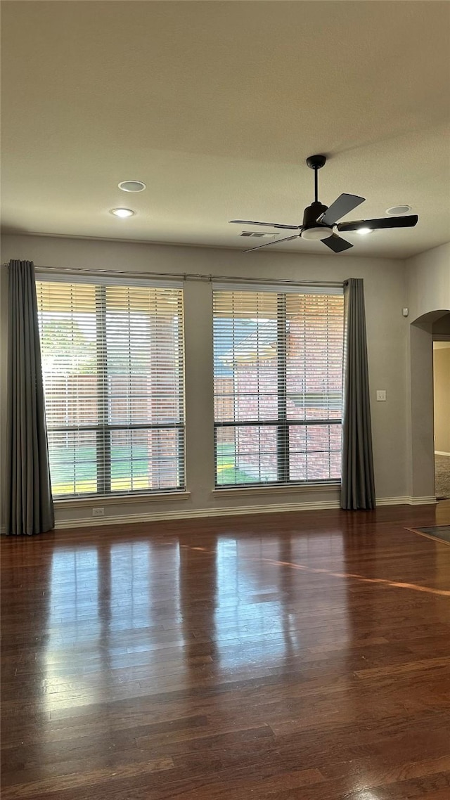 unfurnished room featuring ceiling fan, arched walkways, wood finished floors, and baseboards