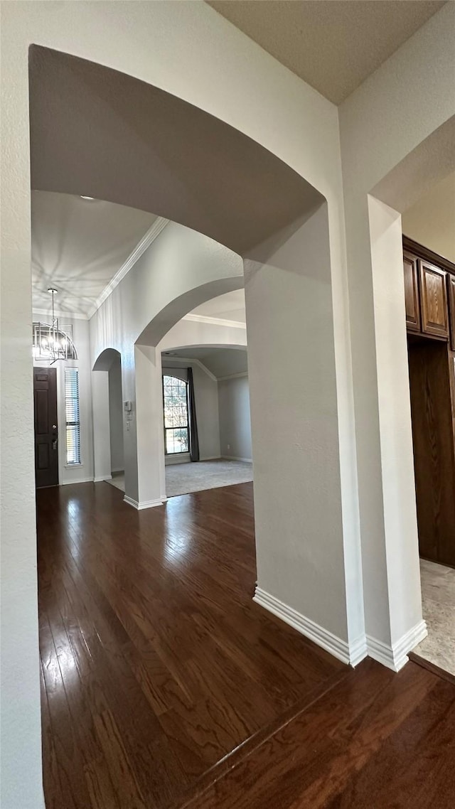 empty room with arched walkways, crown molding, baseboards, and wood finished floors