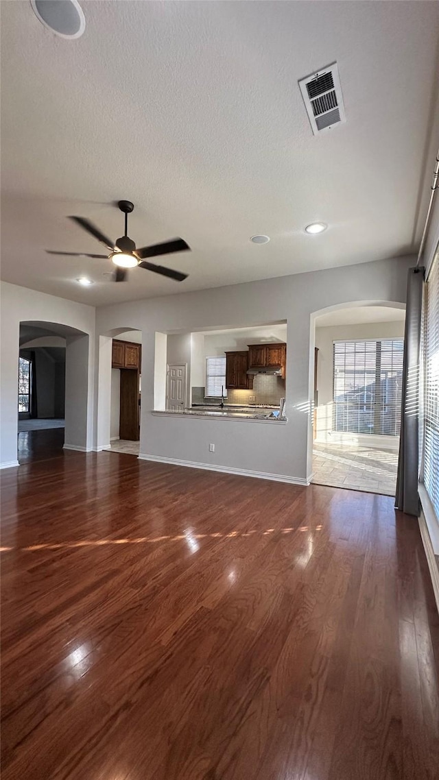 unfurnished living room with visible vents, arched walkways, a ceiling fan, dark wood-style flooring, and a textured ceiling