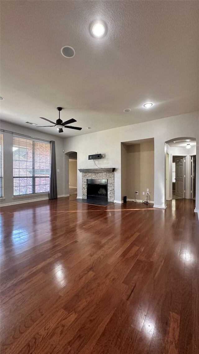 unfurnished living room with arched walkways, baseboards, wood-type flooring, ceiling fan, and a fireplace with flush hearth