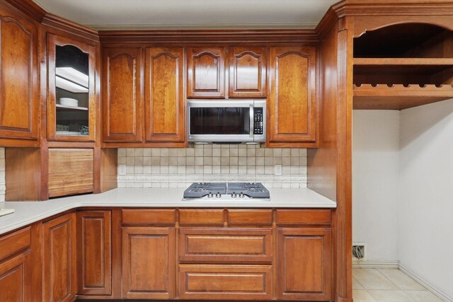 kitchen with light countertops, stainless steel microwave, brown cabinetry, and decorative backsplash