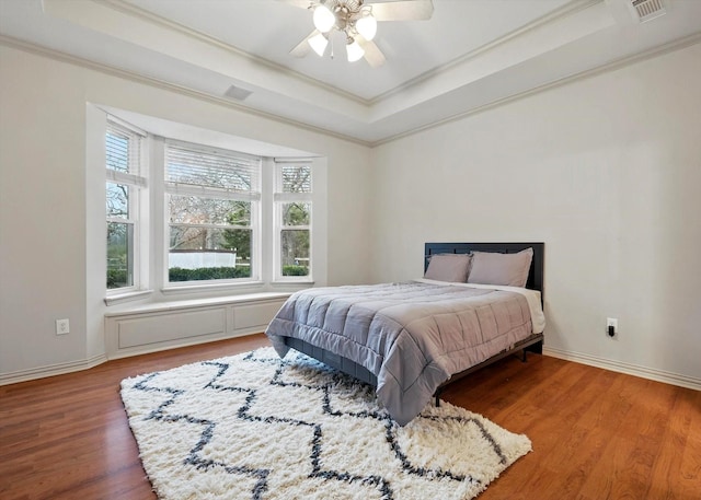 bedroom with baseboards, ornamental molding, a raised ceiling, and wood finished floors