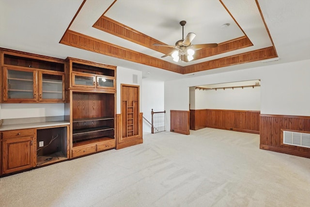 interior space featuring light carpet, wooden walls, visible vents, a raised ceiling, and a wainscoted wall