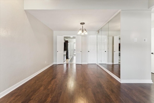 unfurnished dining area featuring baseboards, a notable chandelier, and wood finished floors