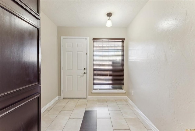 doorway featuring light tile patterned floors, baseboards, and a textured wall