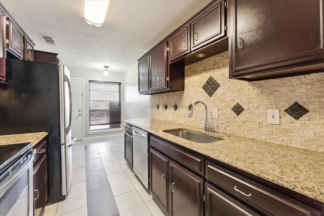 kitchen with a sink, light stone counters, backsplash, stainless steel appliances, and dark brown cabinetry