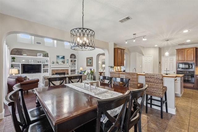 dining space with a chandelier, visible vents, a fireplace, and built in features