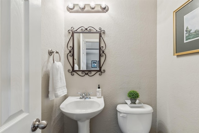 half bath featuring toilet, a sink, and a textured wall