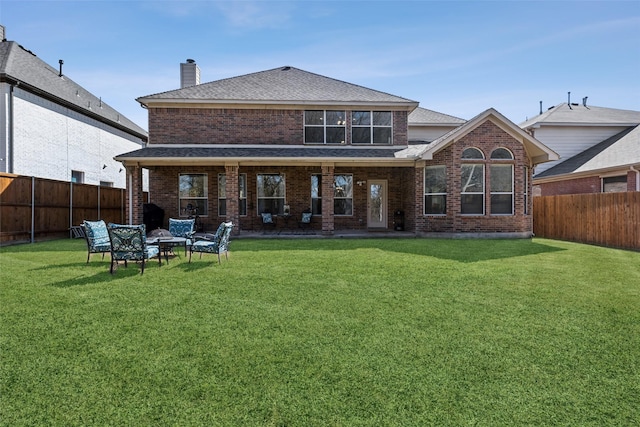 rear view of property featuring a chimney, brick siding, a lawn, and a fenced backyard