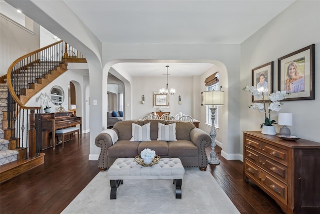 living room with arched walkways, hardwood / wood-style flooring, baseboards, stairway, and an inviting chandelier