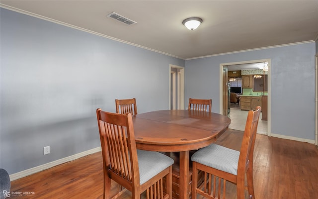 dining space featuring ornamental molding, wood finished floors, visible vents, and baseboards