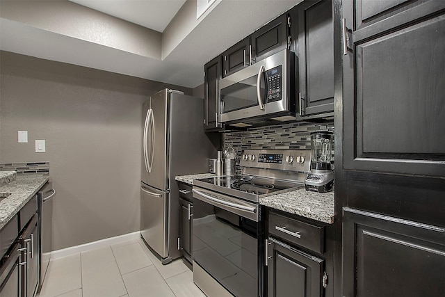 kitchen with light tile patterned floors, light stone counters, baseboards, appliances with stainless steel finishes, and backsplash