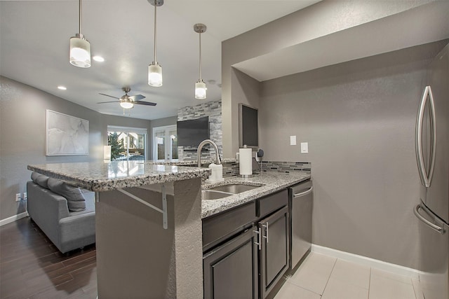 kitchen with light stone counters, a sink, open floor plan, hanging light fixtures, and appliances with stainless steel finishes