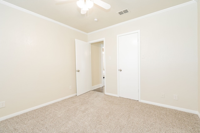 carpeted spare room with visible vents, crown molding, baseboards, and ceiling fan