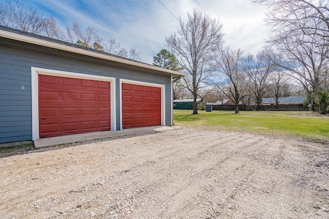 garage featuring dirt driveway and fence