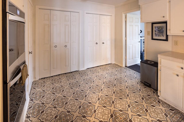 kitchen with ornamental molding, tile counters, and white cabinetry