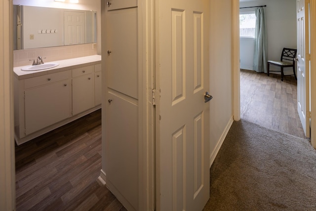 hallway with dark wood-style floors, baseboards, and a sink