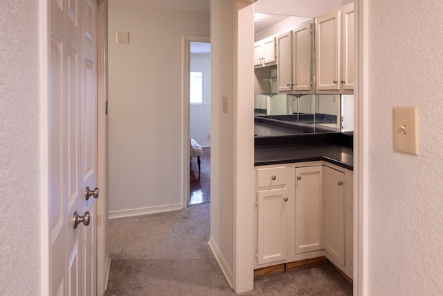 corridor featuring baseboards, dark colored carpet, and a textured wall